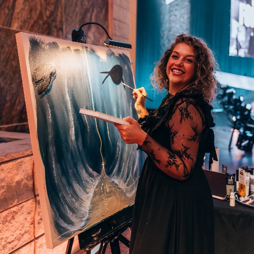 woman smiling at a canvas with a paint brush in hand